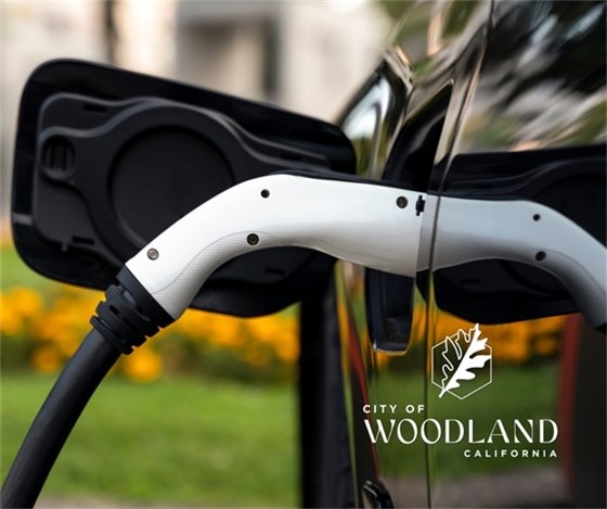 Image of an electric vehicle plugged in to a charger with the City of Woodland logo at bottom right