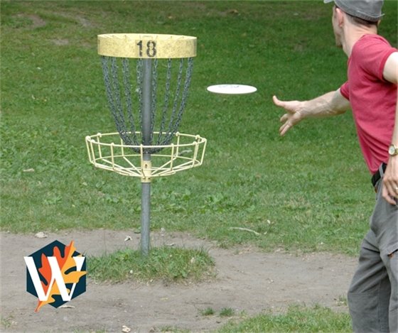 Disc golfer throwing disc at basket with City "W" logo in bottom left