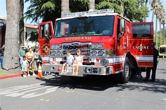 Two children sitting on the front bumper of a Woodland Fire Truck